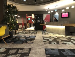 A reception area with a modern design, featuring a reception desk, seating area with chairs, and a large potted plant. - ibis Lyon Caluire Cité Internationale (Caluire-et-Cuire)