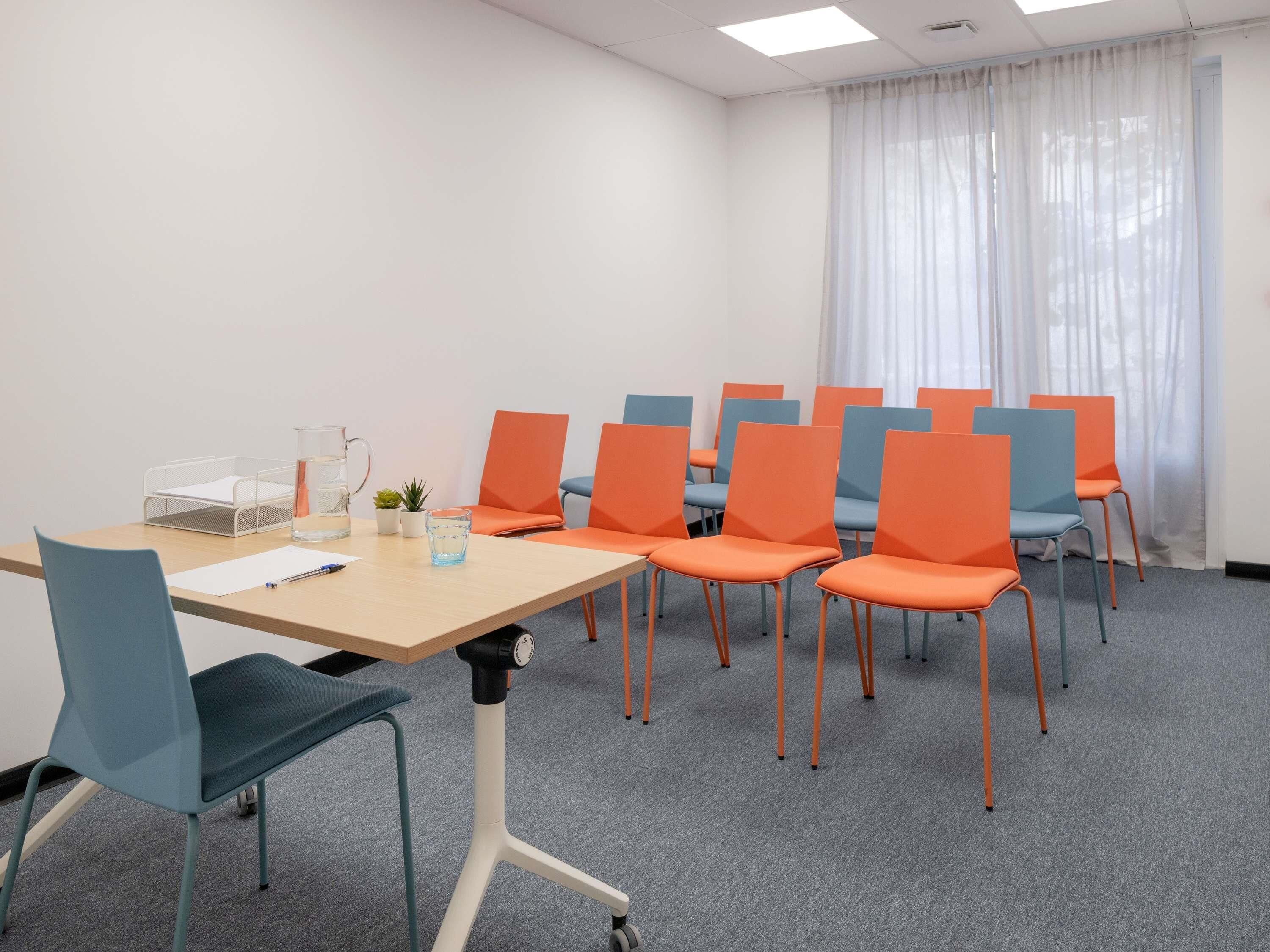 A conference room with a long table, multiple chairs, a clock, and a window with curtains.