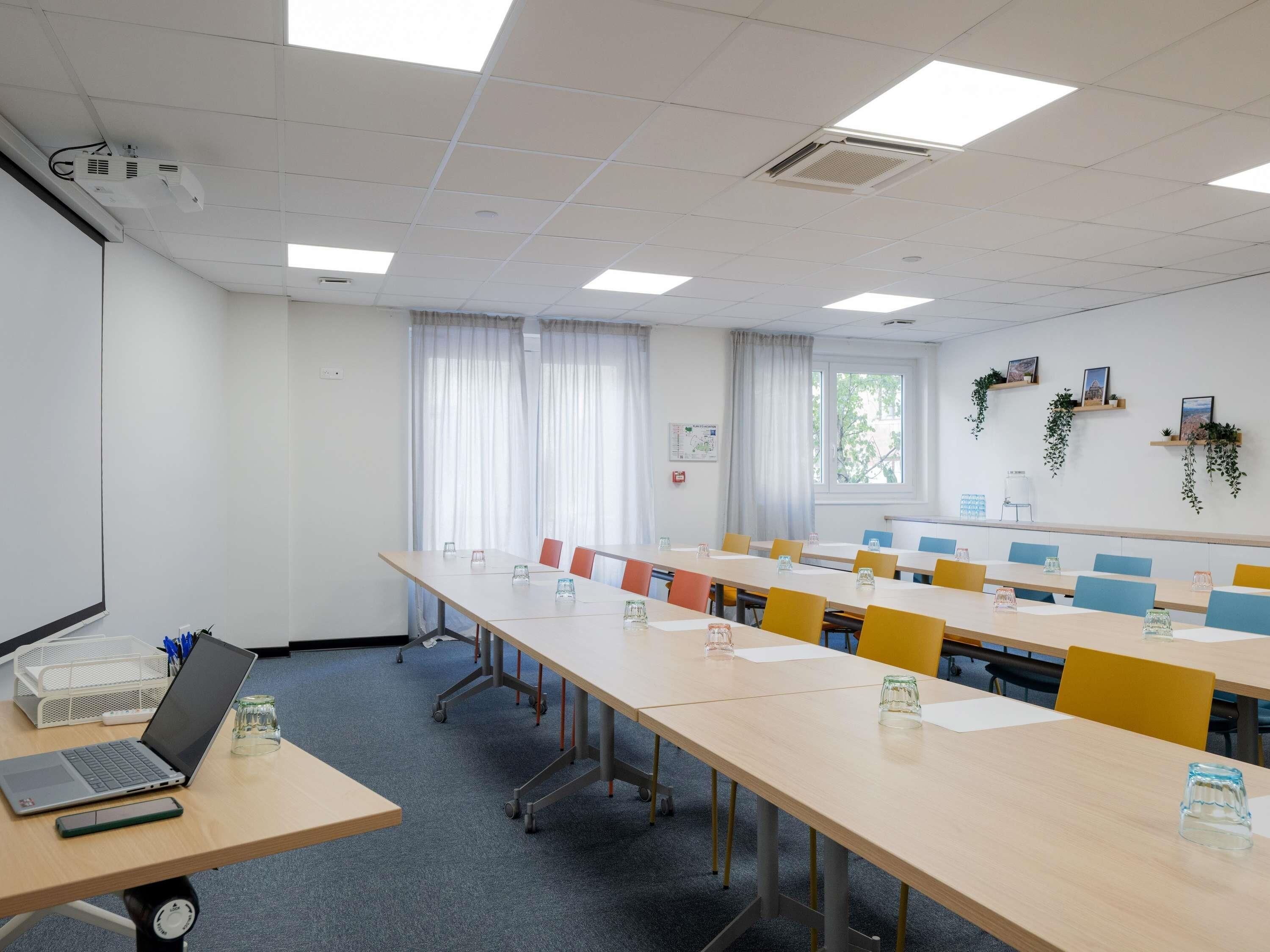 Un salón de conferencias con una larga mesa, sillas, un proyector y una ventana con cortinas.