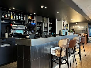 A modern bar area with a coffee machine, shelves of liquor bottles, and bar stools. - ibis Lyon Caluire Cité Internationale (Caluire-et-Cuire)