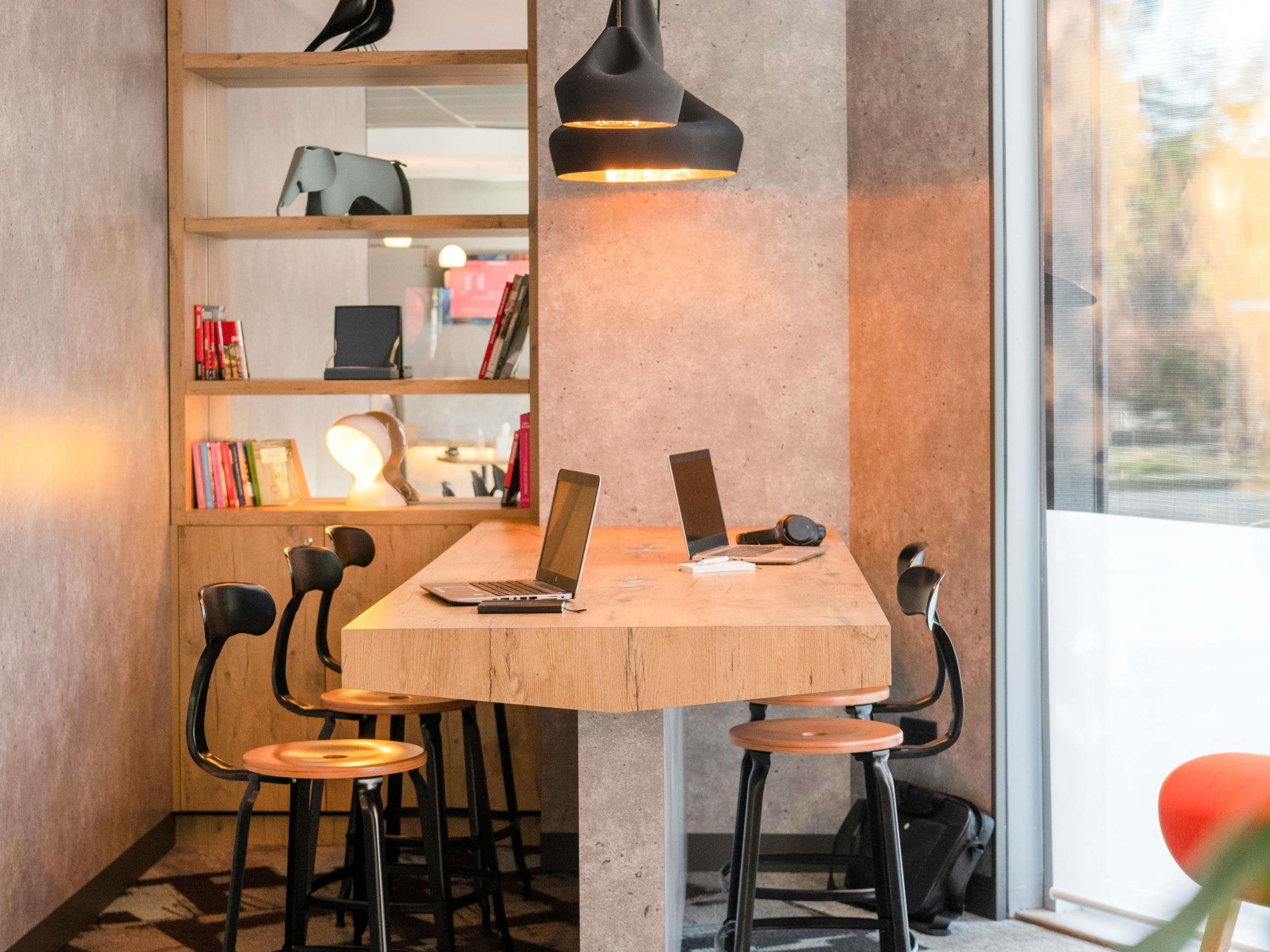Un espace de travail avec une table en bois, deux ordinateurs portables, une lampe et une bibliothèque remplie de livres, ainsi qu’une chaise.