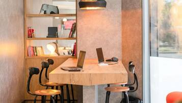 Un espace de travail avec une table en bois, deux ordinateurs portables, une lampe et une bibliothèque remplie de livres, ainsi qu’une chaise.