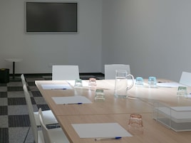 A conference room with a long table, chairs, a whiteboard, and various items like glasses and a water pitcher.