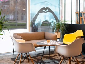 A modern interior with a sofa, two chairs, a small table, and a large window with a heart-shaped decoration. - ibis Lyon Caluire Cité Internationale (Caluire-et-Cuire)