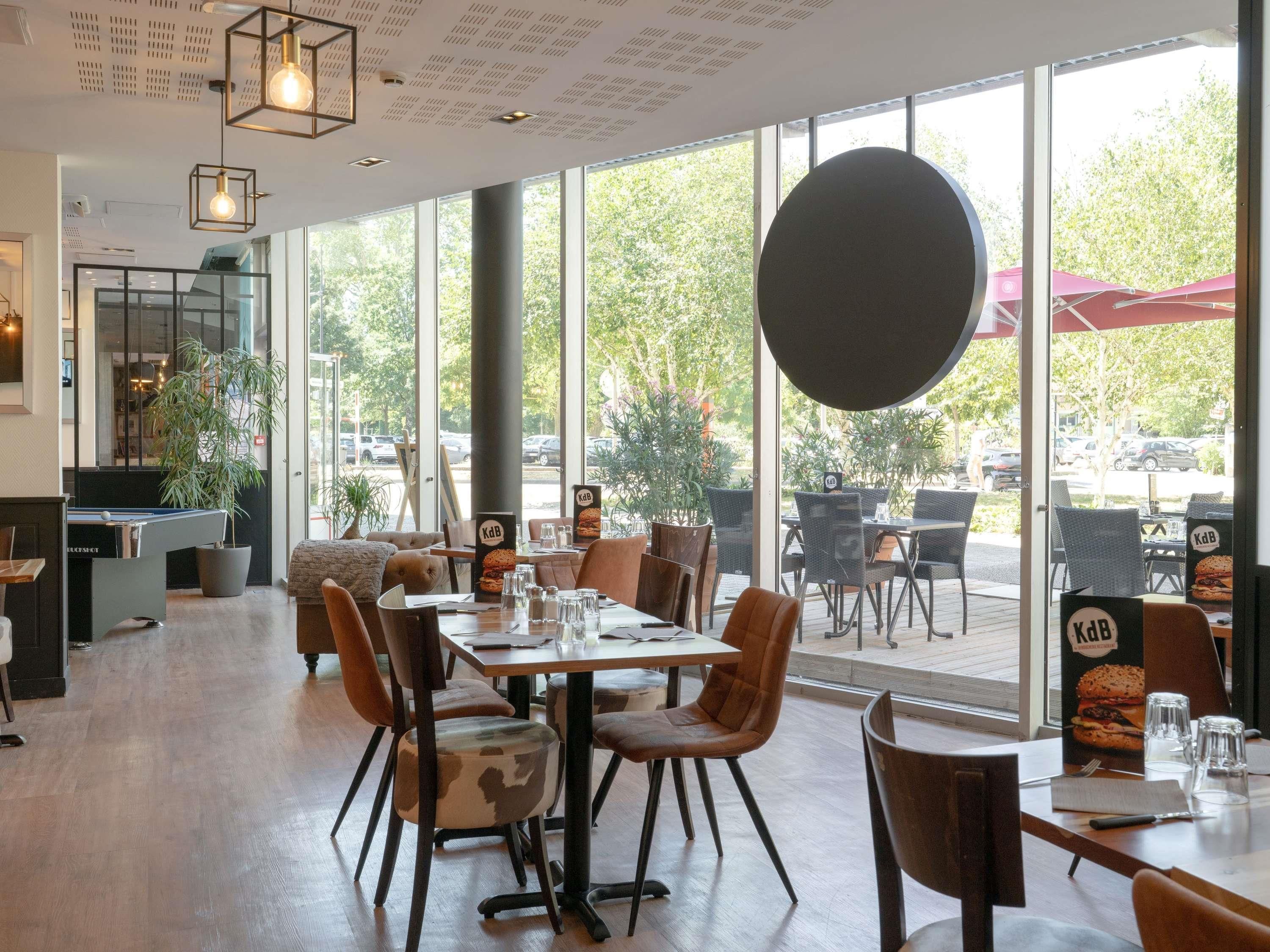 Un espace de restauration intérieur avec des tables et des chaises, de grandes fenêtres et une vue sur l’extérieur.