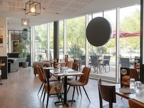 An indoor dining area with tables and chairs, large windows, and a view of the outdoors.