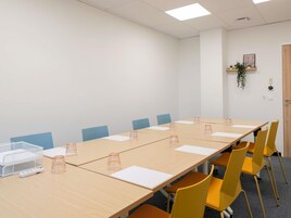 Un salón de conferencias con una mesa grande, sillas amarillas y una pizarra.
