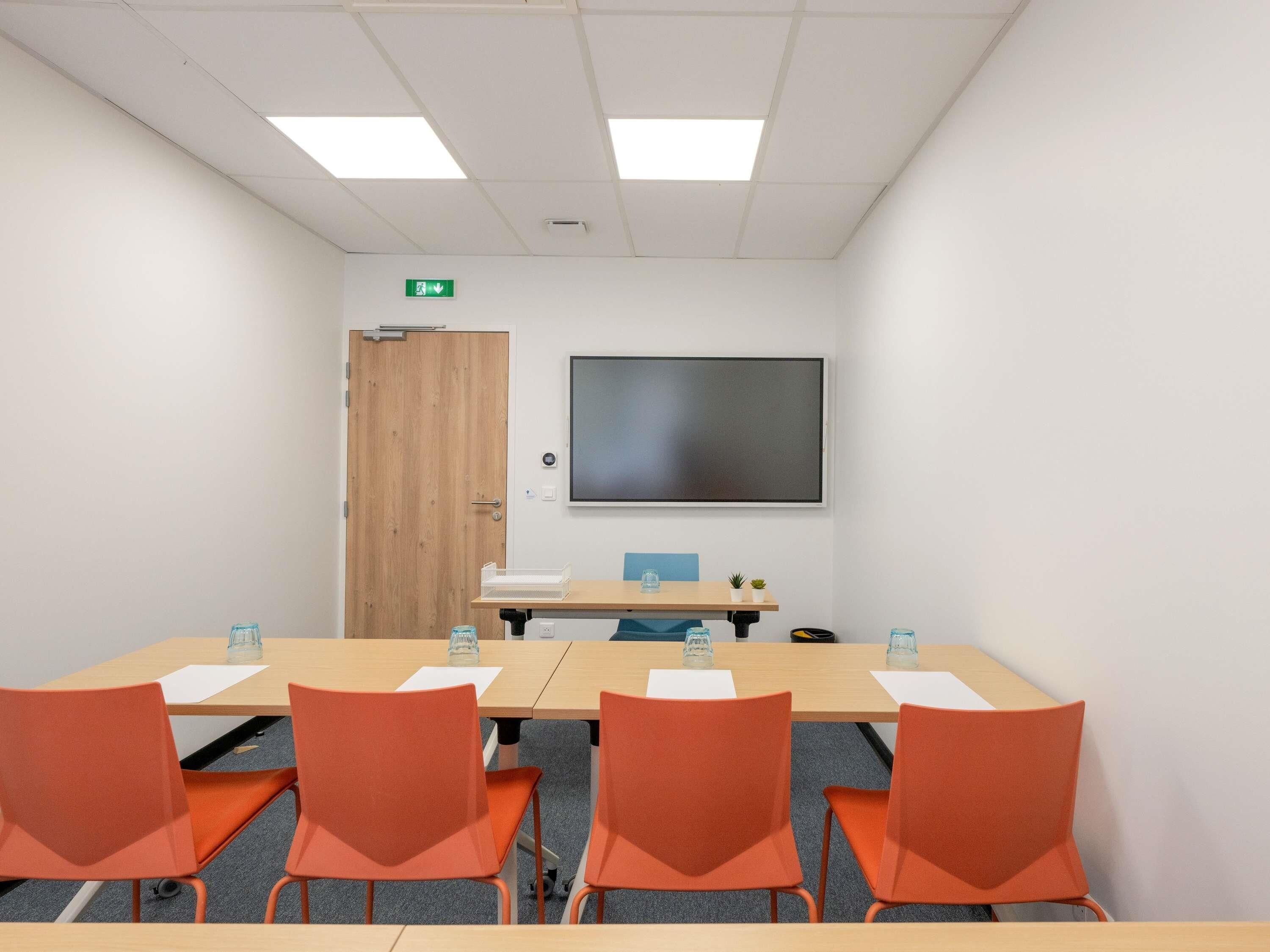 A conference room with a large screen, a wooden door, and orange chairs.