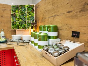 A kitchen area with green tea canisters, a wooden wall with a green plant wall, and a sign indicating 'Tea'. - ibis Lyon Caluire Cité Internationale (Caluire-et-Cuire)