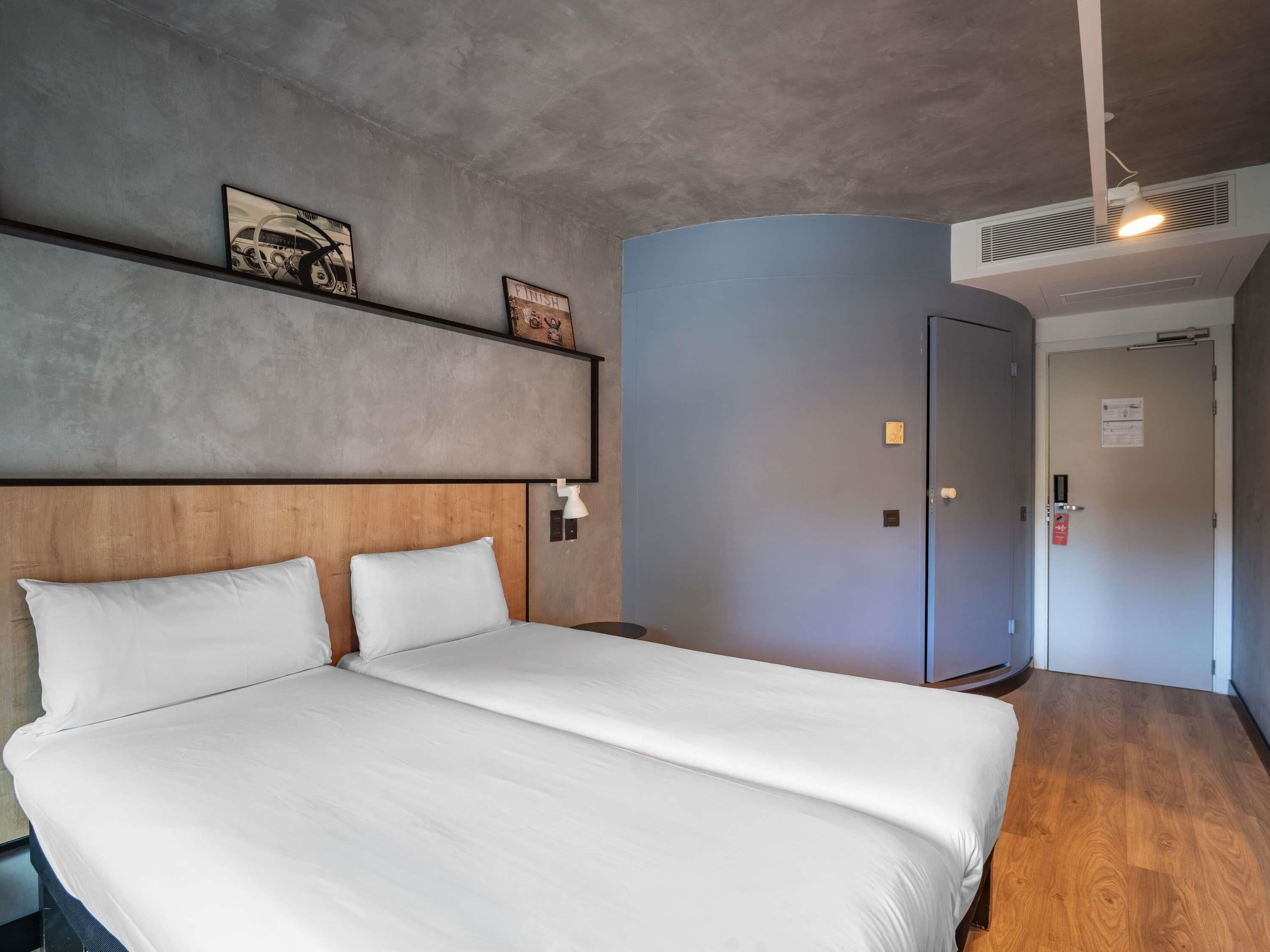 A hotel room with a large bed, a wooden headboard, a grey accent wall, and a door with a lock.