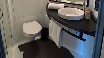 A bathroom with a toilet, a sink, a mirror, and a black trash bin.