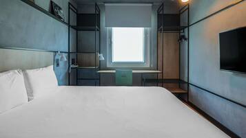 Une chambre d’hôtel avec un lit, un bureau, une chaise, une fenêtre et un téléviseur.