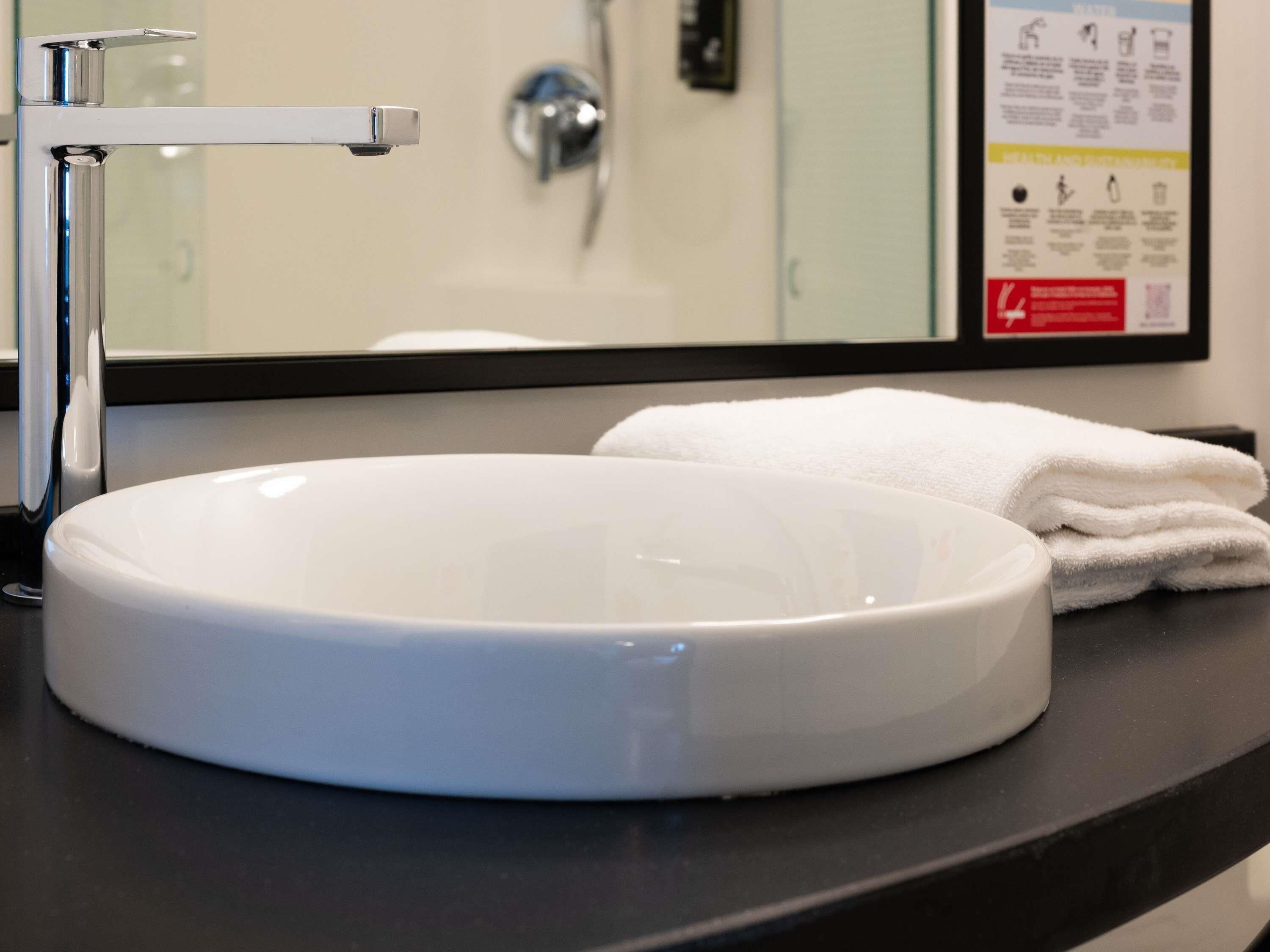 A white sink with a chrome faucet, a mirror above it, and a folded white towel on the counter.