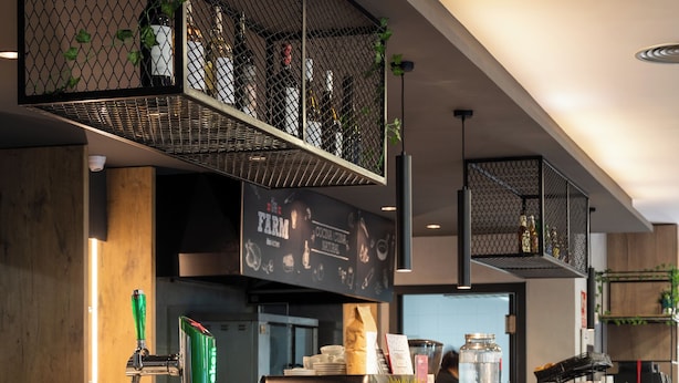 A modern bar area with a wooden counter, metal chairs, and a variety of bottles and plants on shelves. - ibis Barcelona Montmelo-Granollers (Granollers)
