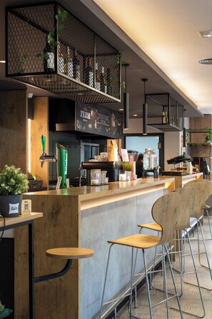A modern bar area with a wooden counter, metal chairs, and a variety of bottles and plants on shelves. - ibis Barcelona Montmelo-Granollers (Granollers)