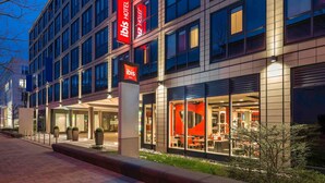 Un hôtel moderne, reconnaissable à son grand panneau rouge et blanc, à ses larges fenêtres et à son espace extérieur bien éclairé, aménagé pour accueillir les clients.