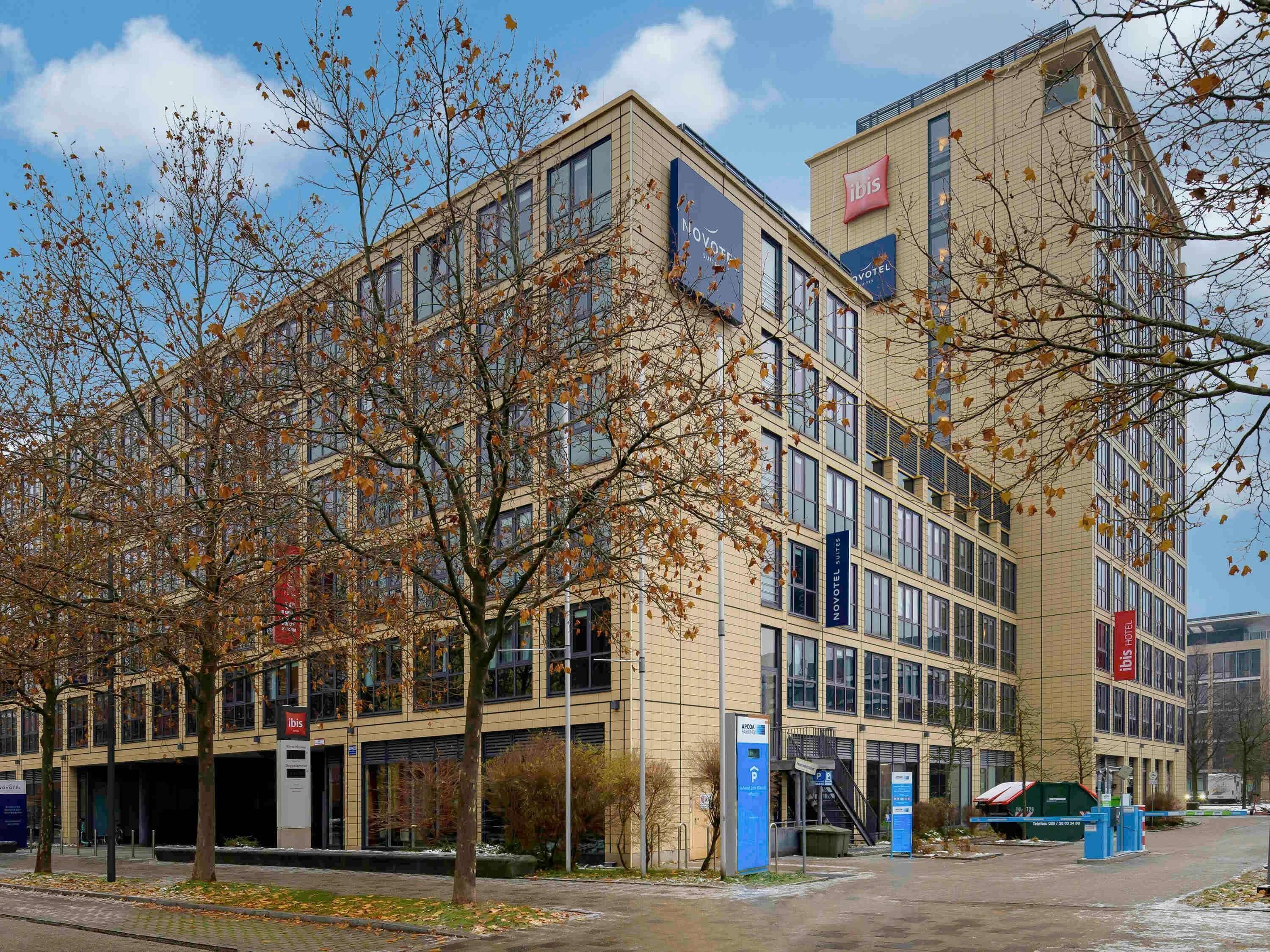 A modern hotel with multiple floors, a prominent "ibis" sign, and a parking area.