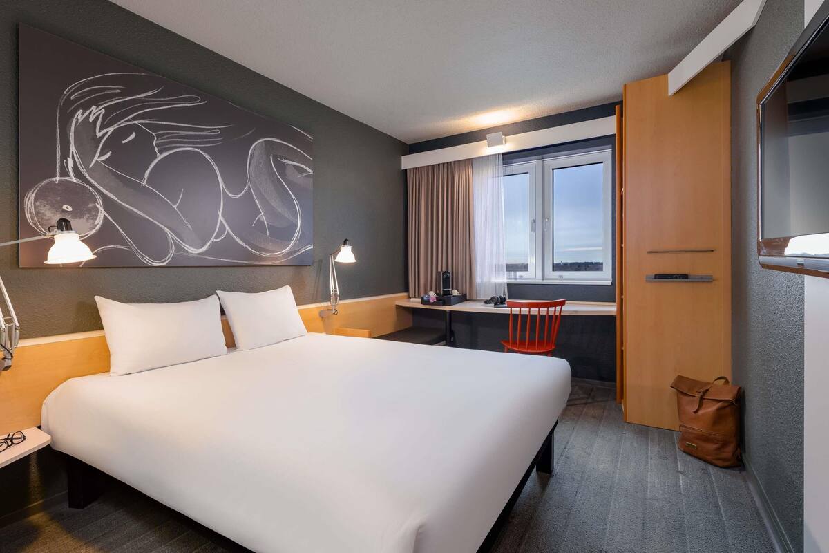 Een hotelkamer met een bed, bureau, stoel en kunst aan de muur.