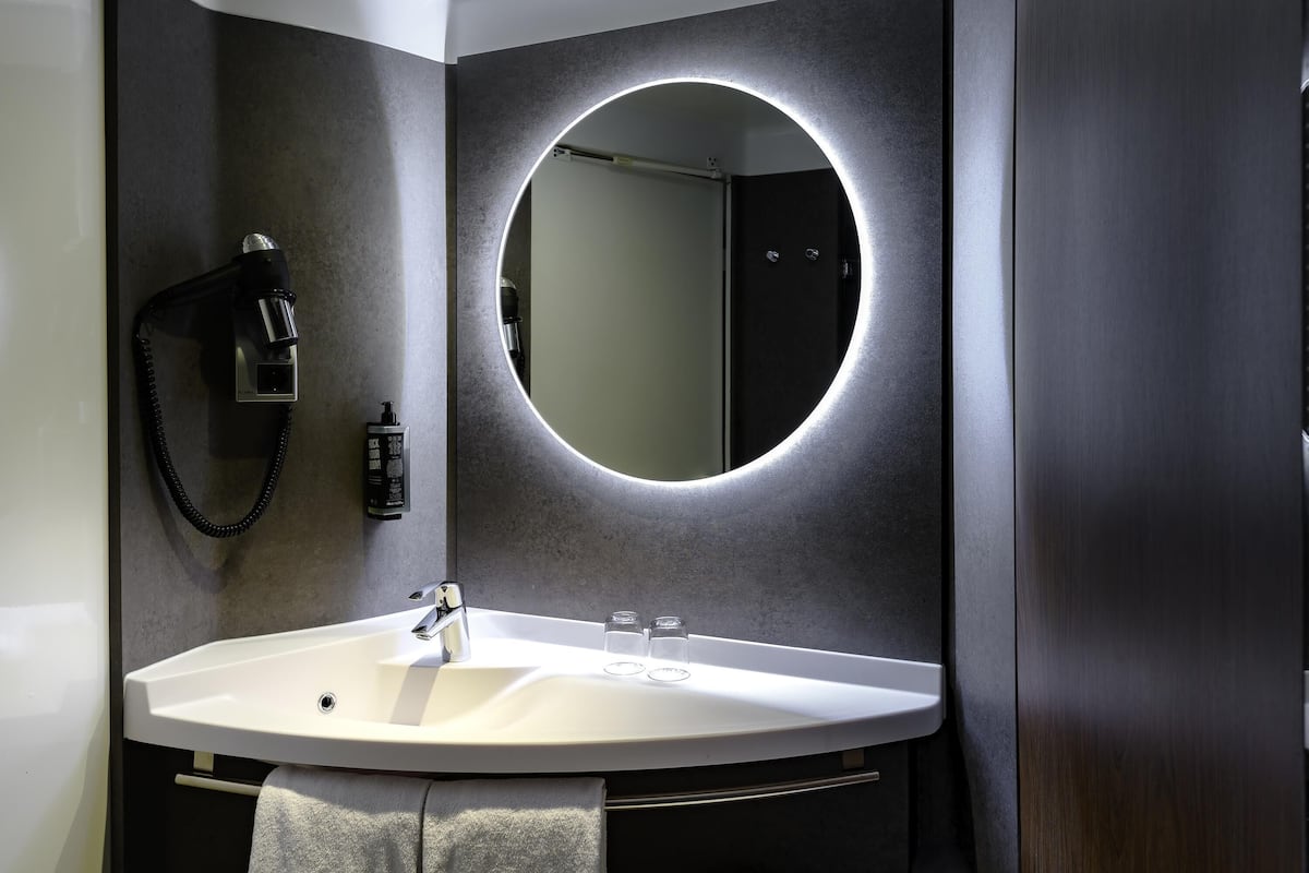 A modern bathroom with a round mirror, a white sink, a handheld showerhead, and a towel rack.
