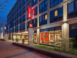 Un hôtel moderne, reconnaissable à son grand panneau rouge et blanc, à ses larges fenêtres et à son espace extérieur bien éclairé, aménagé pour accueillir les clients.