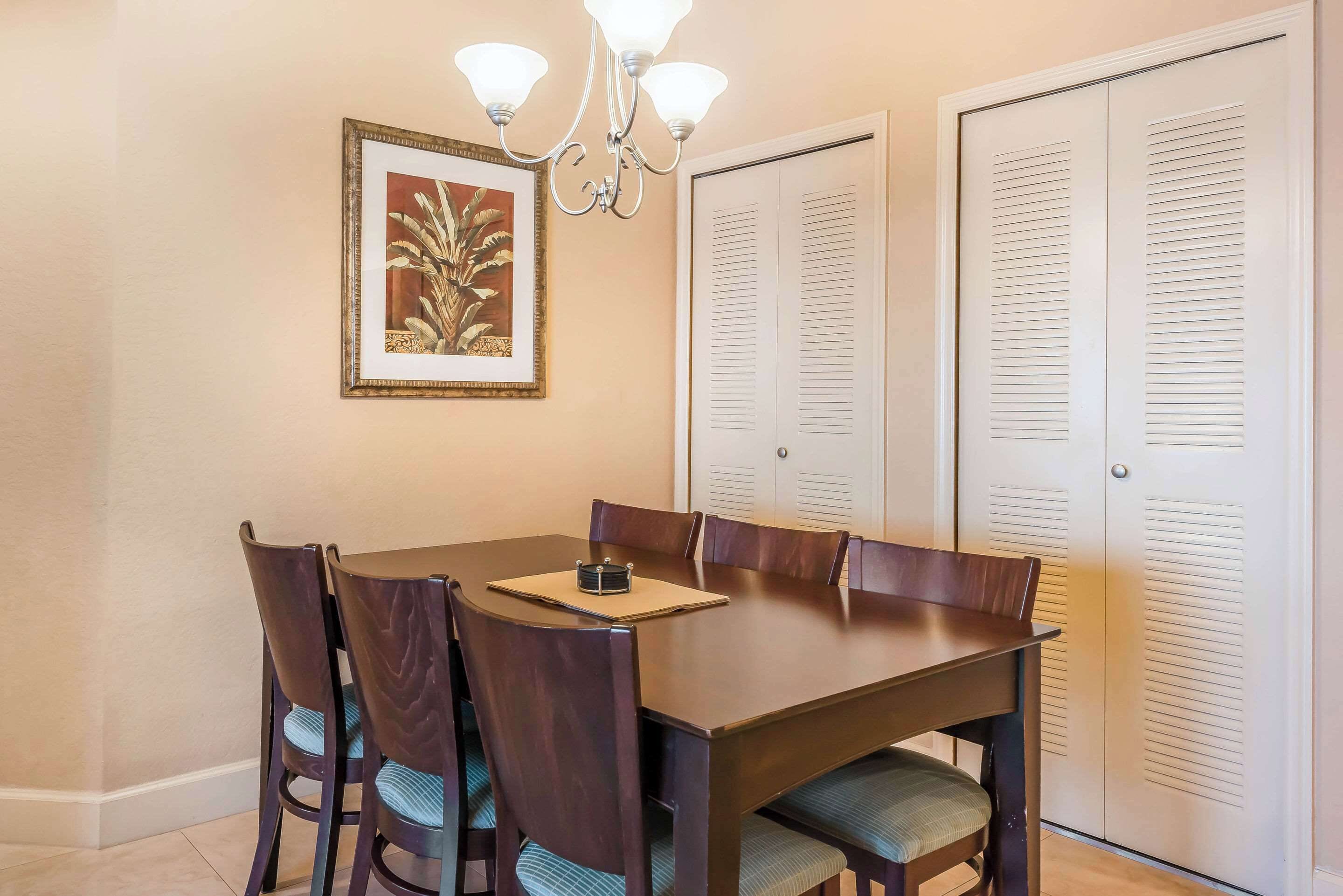 A dining area with a table and chairs, a chandelier, a framed picture, and a set of closets.