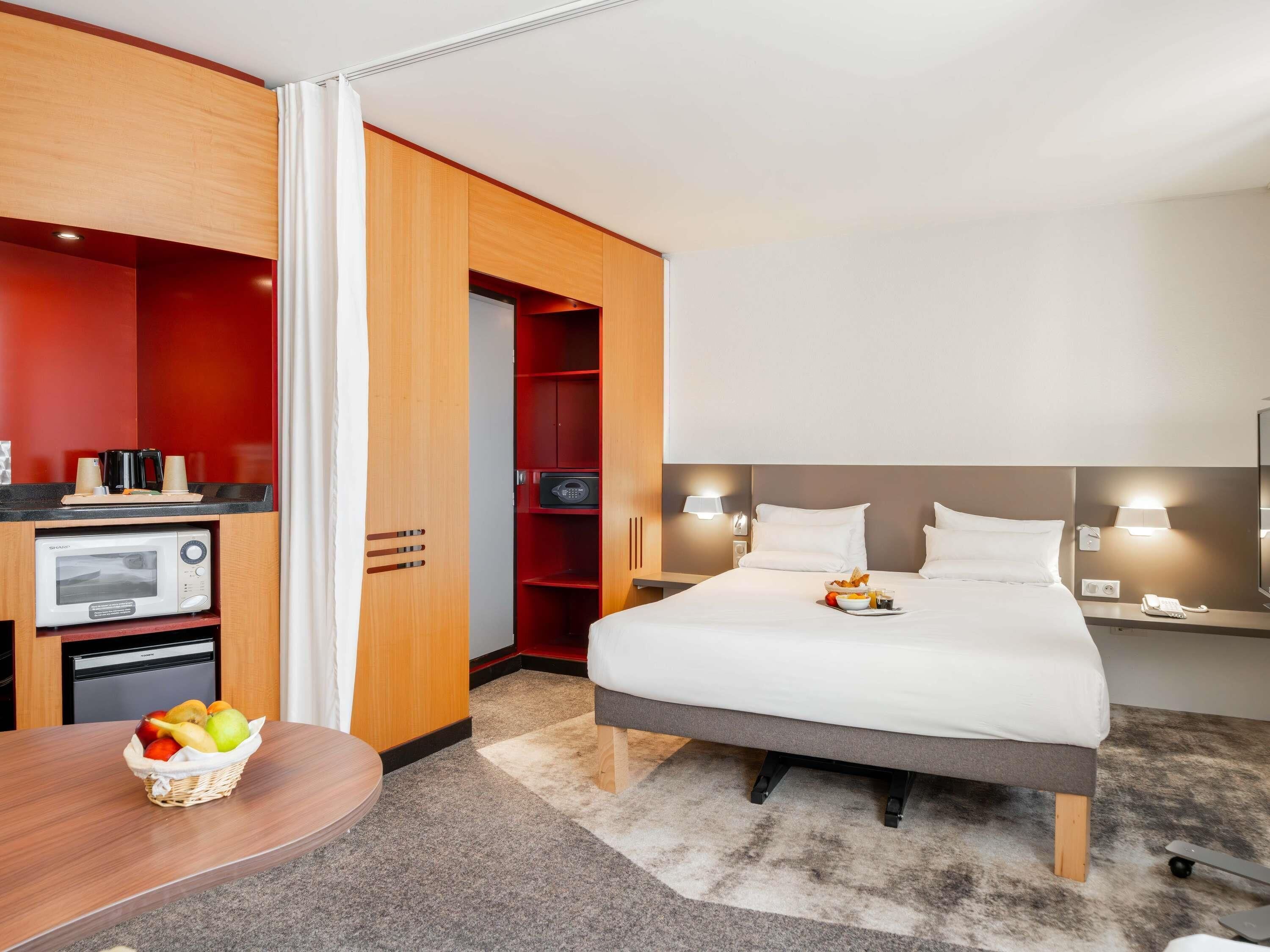 A hotel room with a bed, bedside table, microwave, and a small kitchenette area.