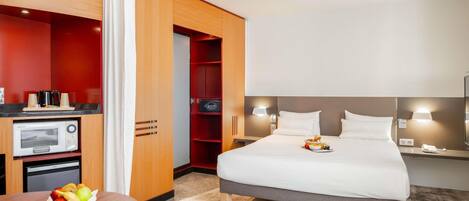 A hotel room with a bed, bedside table, microwave, and a small kitchenette area.