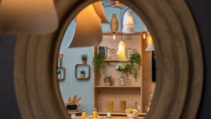 A round mirror with a wooden frame reflecting a kitchen area with shelves, plants, and kitchenware. - Novotel Suites Cannes Centre (Cannes)
