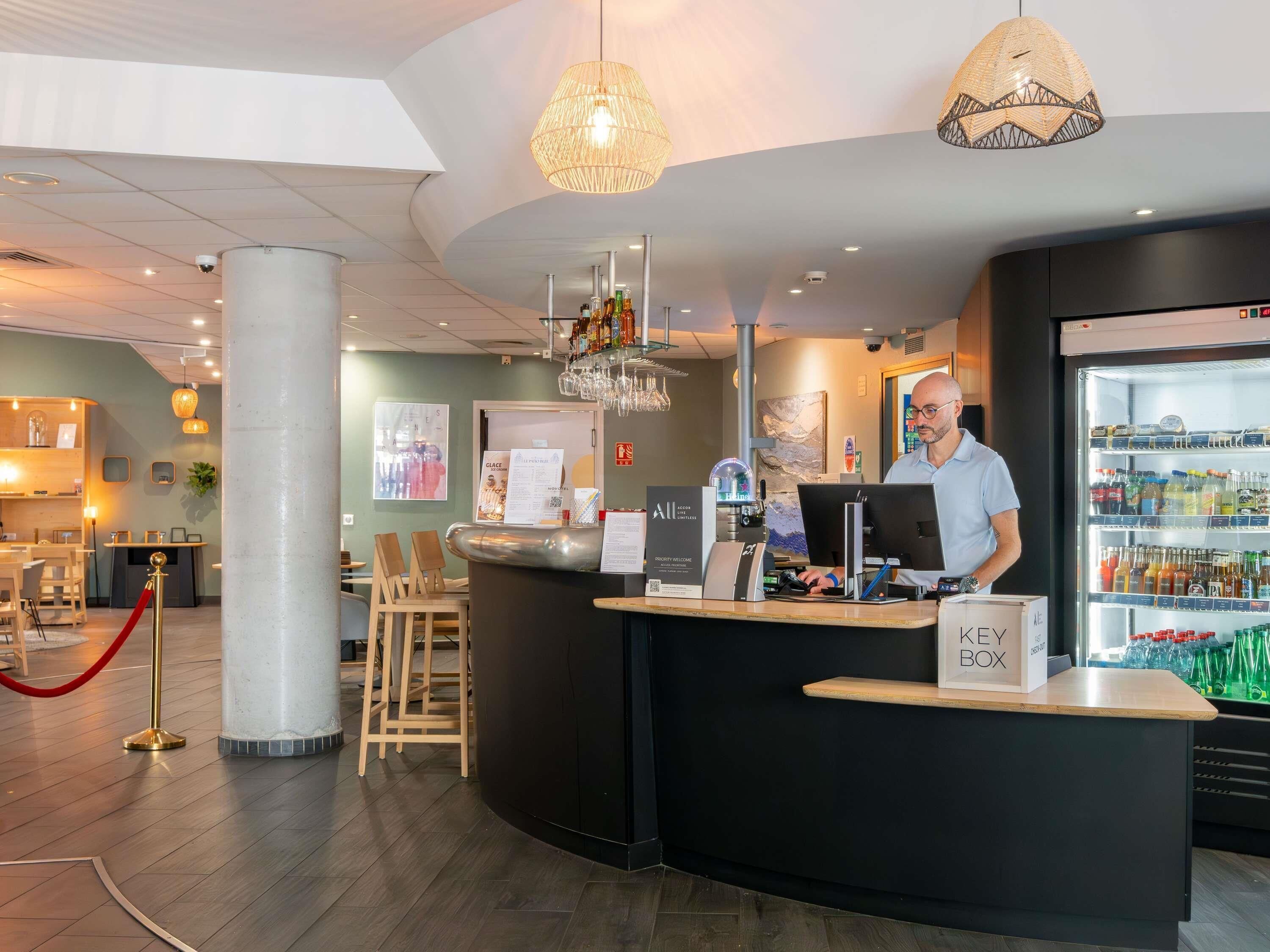 Un espace d’accueil d’hôtel comprenant un comptoir, un ordinateur et un réfrigérateur rempli de boissons.