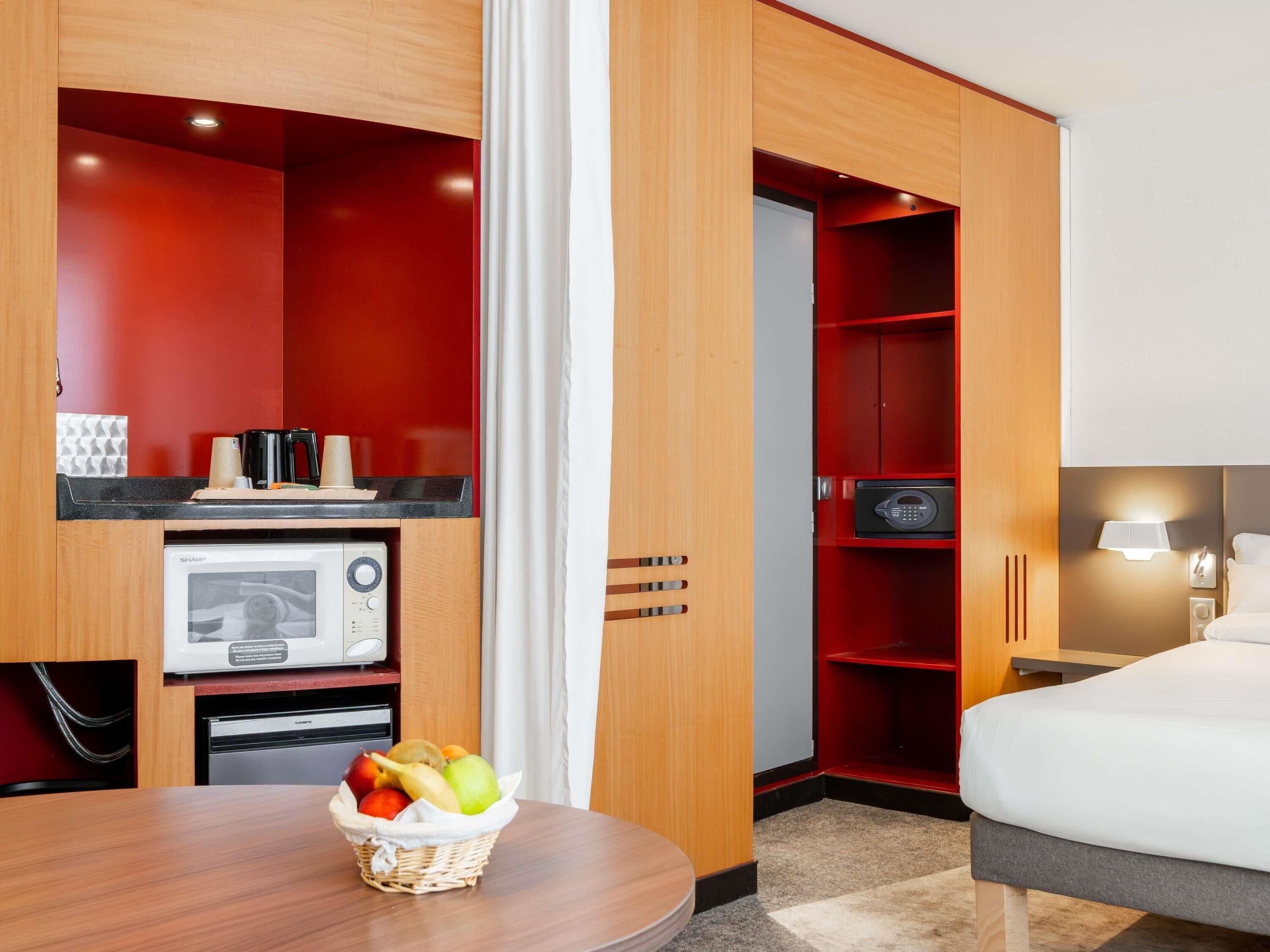 A hotel room with a bed, a desk with a microwave, a coffee maker, and a fruit basket.