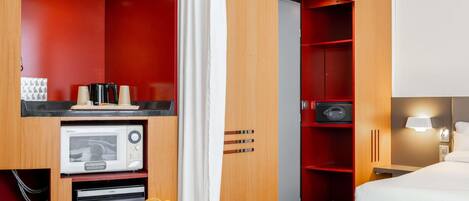 A hotel room with a bed, a desk with a microwave, a coffee maker, and a fruit basket.