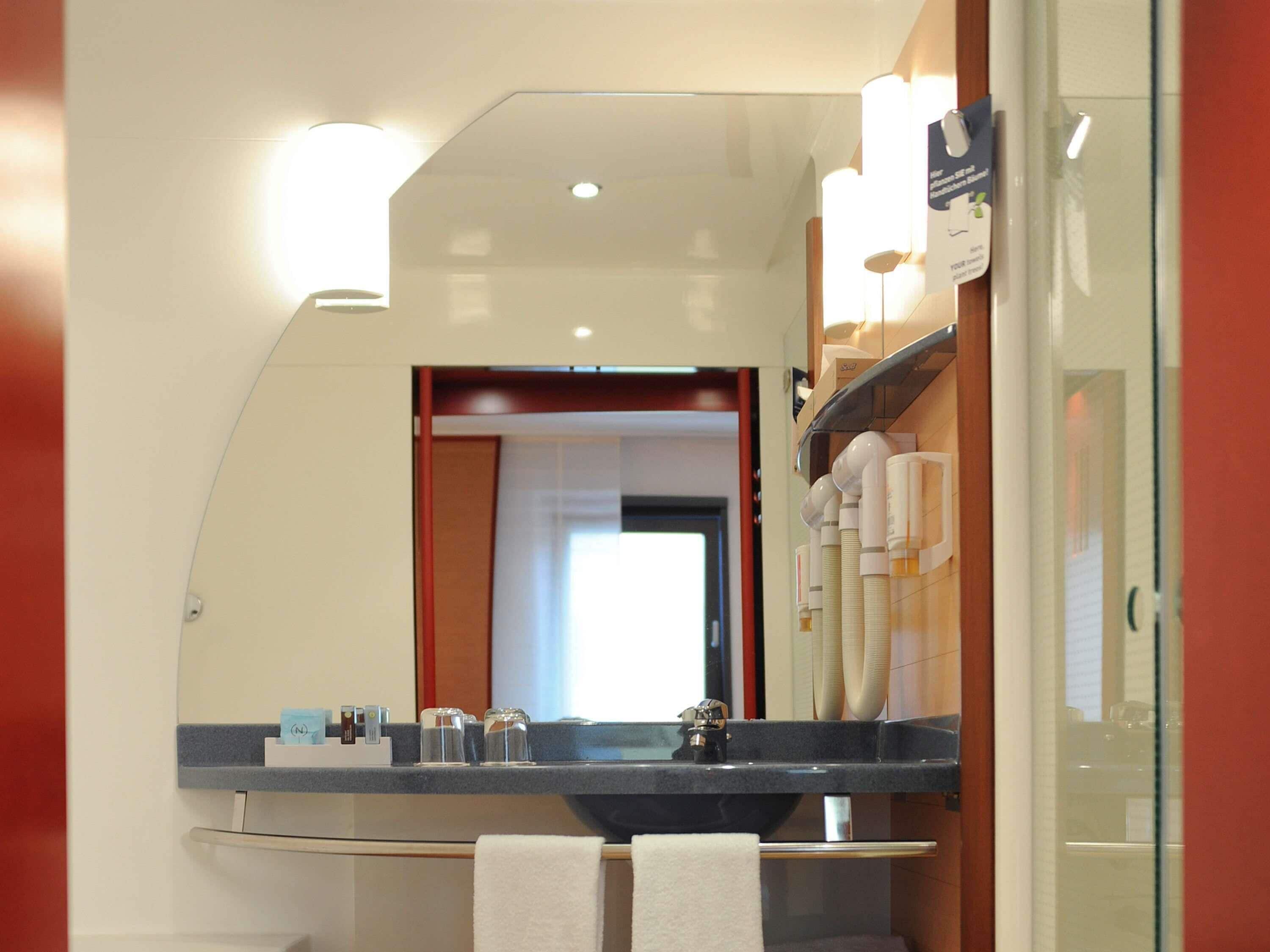 A bathroom with a mirror, sink, towel rack, and toiletries.