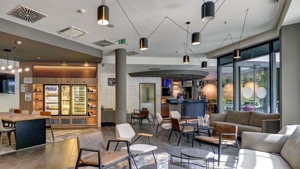 Un moderno vestíbulo de hotel con áreas de estar, un bar y un refrigerador con productos.