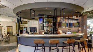 Un área de bar moderna con una barra curva, taburetes y una variedad de botellas y vasos en estantes.