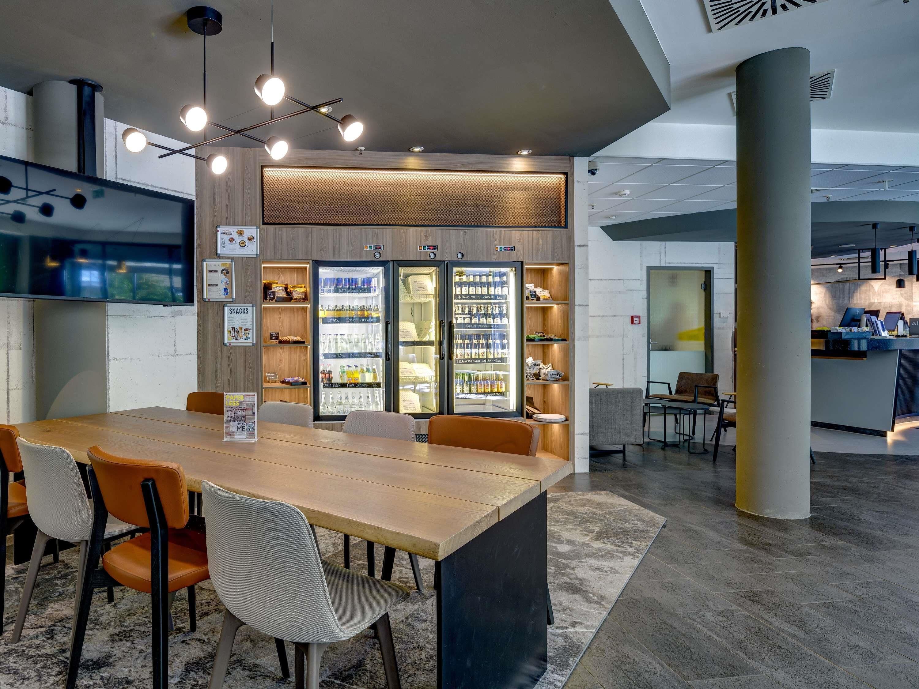 Un interior modern amb una zona de dinar central, un refrigerador ple de begudes i un taulell amb un ordinador.