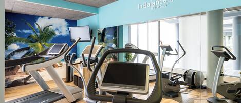 A fitness center with treadmills, ellipticals, and a wall mural.