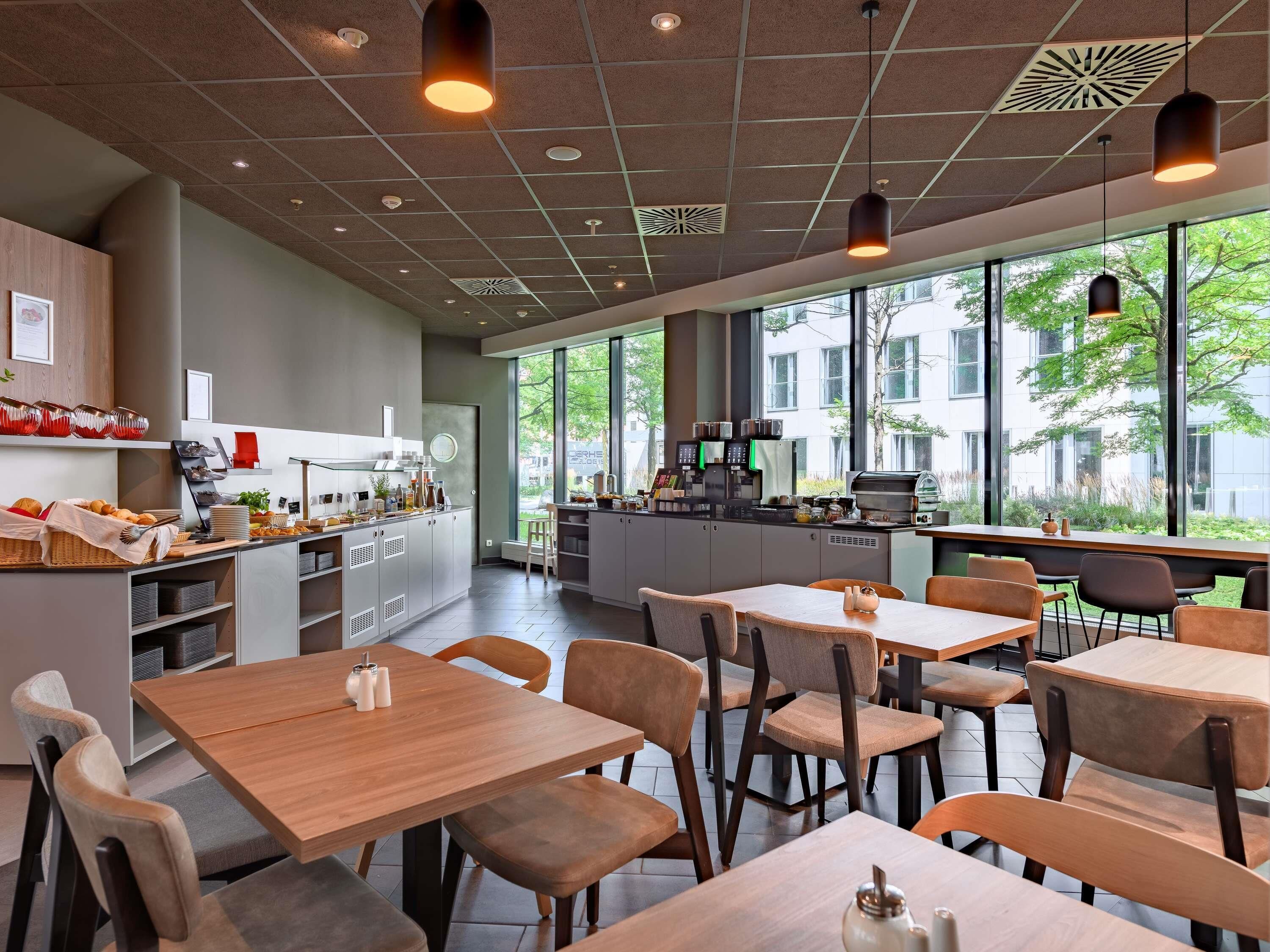 Un café moderno con mesas y sillas de madera, una barra de café y ventanas amplias que ofrecen vistas al exterior.