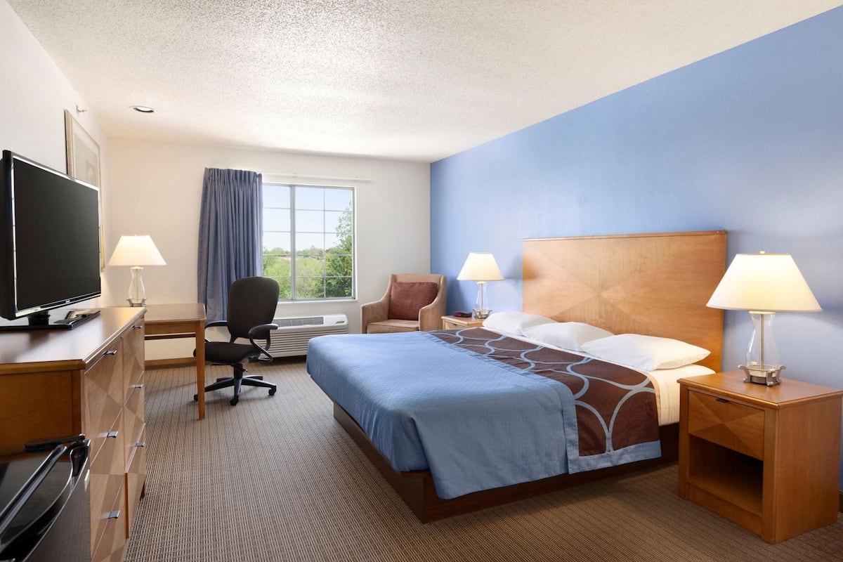 A hotel room with a bed, two bedside tables with lamps, a desk with a TV, a chair, and a window with curtains.