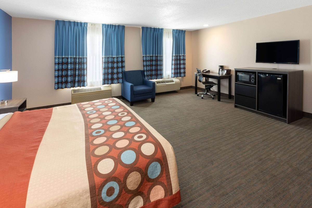 A hotel room with a bed, a desk with a computer, a TV, and a kitchenette.