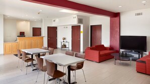 Un salon moderne avec un coin repas, des canapés rouges, un téléviseur et une cuisine en arrière-plan.