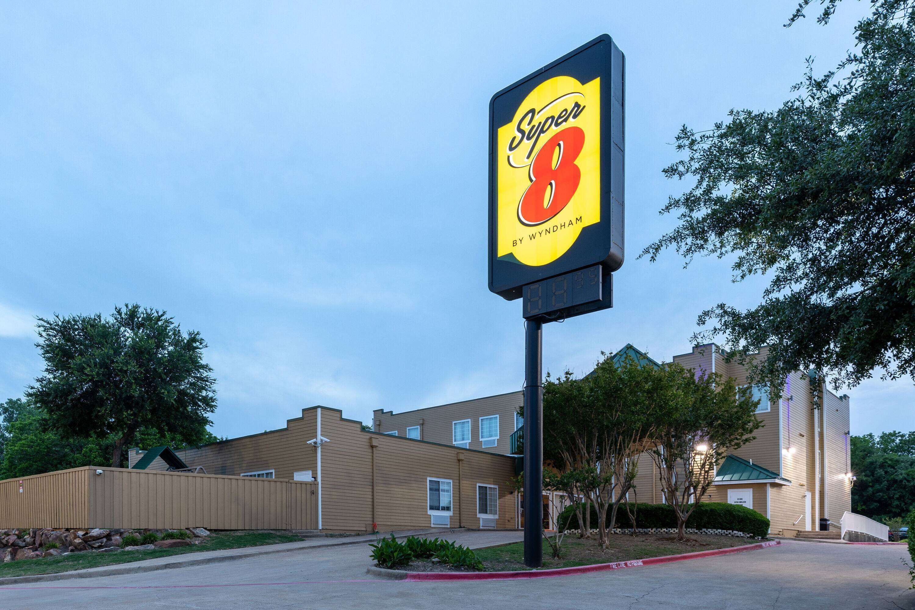 Señal de un hotel Super 8 by Wyndham con un edificio moderno al fondo.