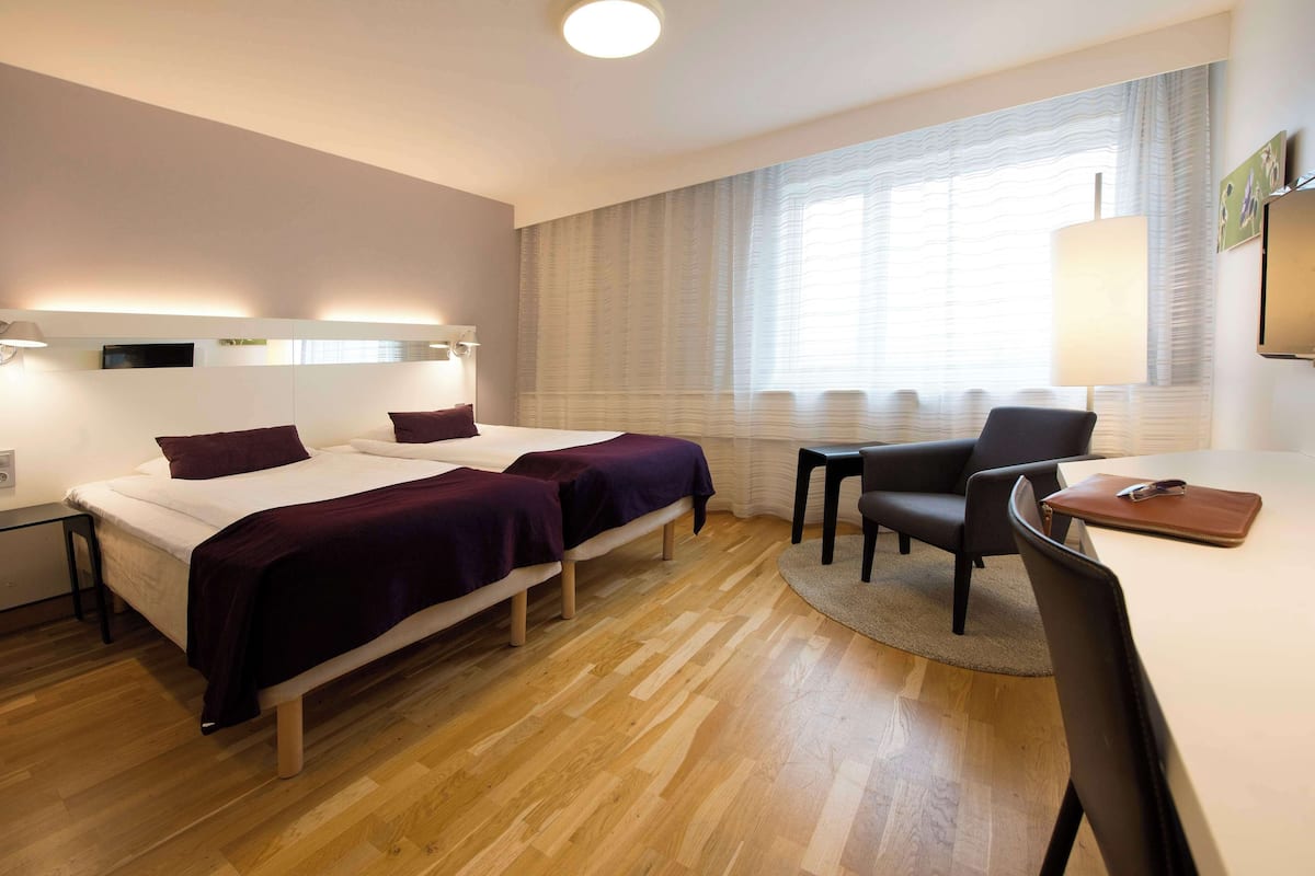 A hotel room with two beds, a desk, and a chair.