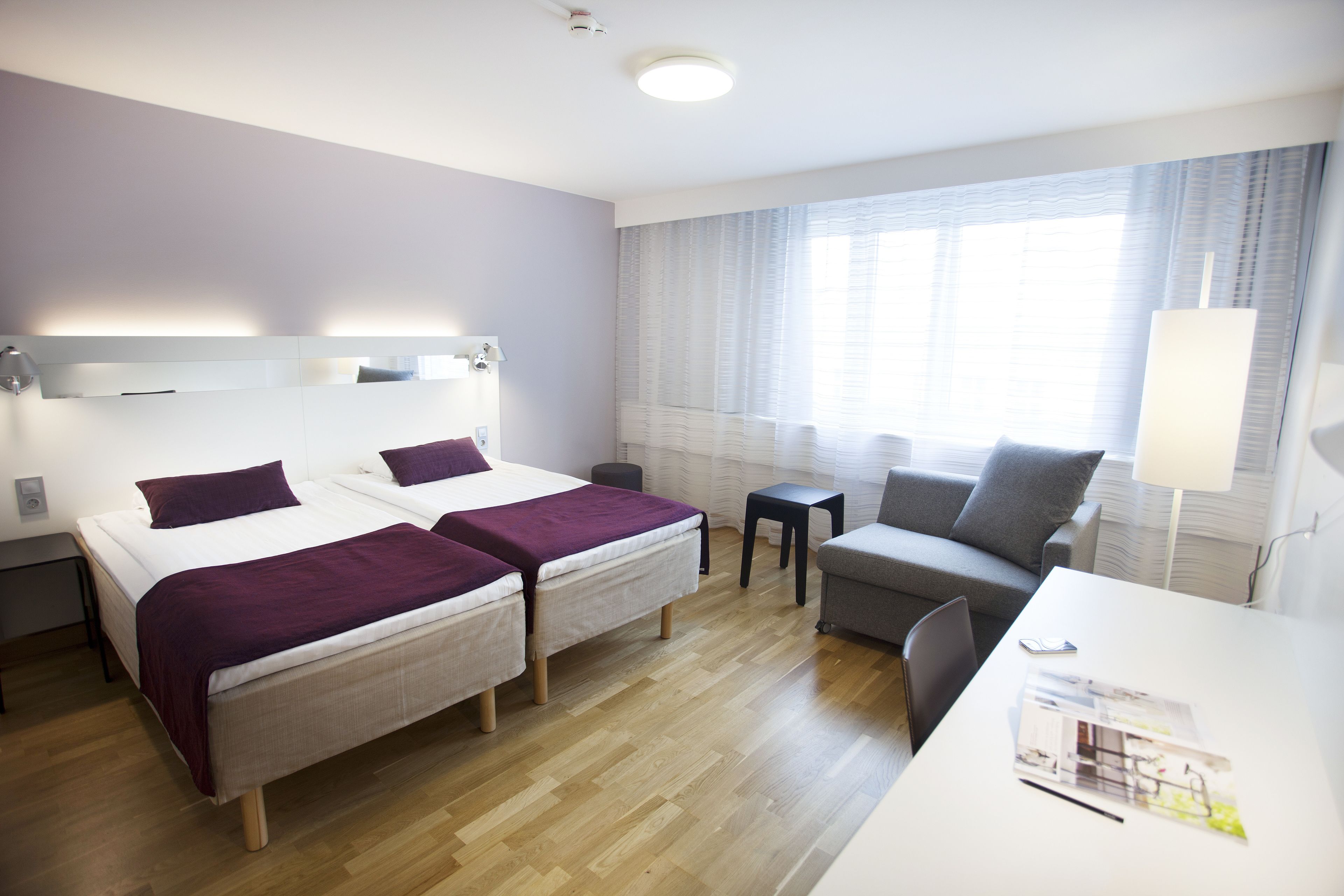 Een hotelkamer met twee bedden, een bureau, een stoel, een klein tafeltje en een lamp.