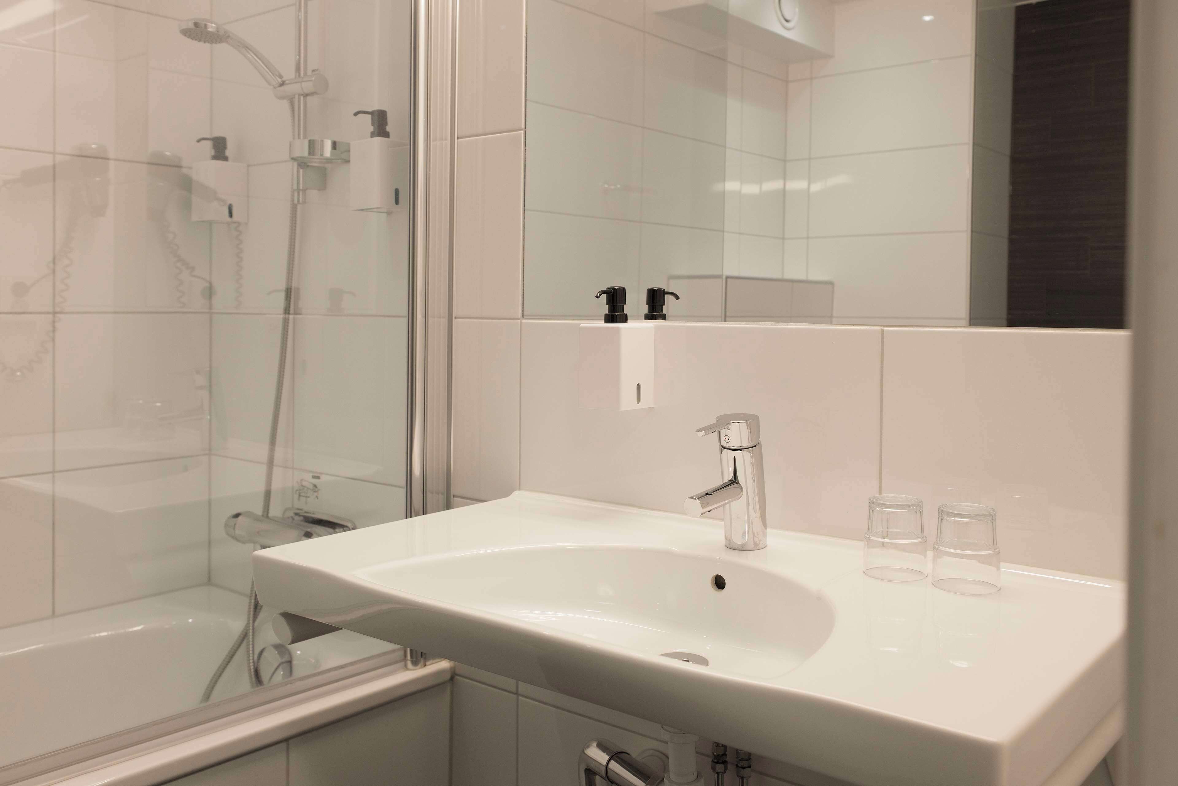 A modern bathroom with a white sink, a glass shower enclosure, and a large mirror.