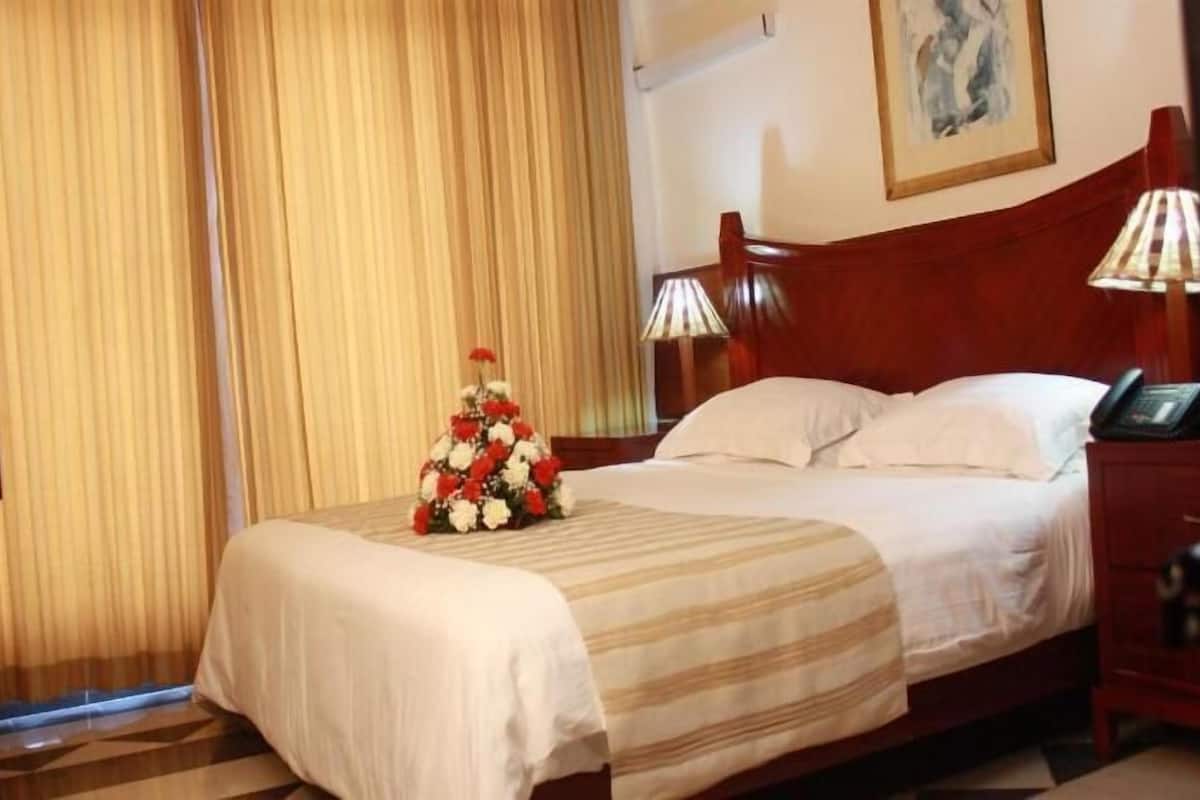 A hotel room with a bed, a television, a lamp, and a floral arrangement.
