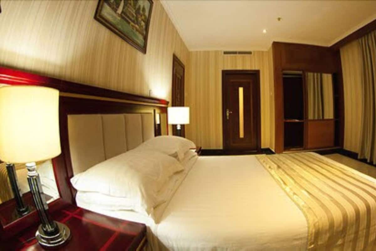 A hotel room with a bed, a nightstand with a lamp, a door, and a window with curtains.