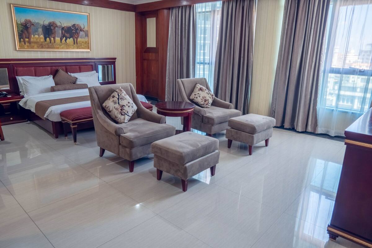 A hotel room with a large bed, two armchairs, a small table, and a large window with curtains.