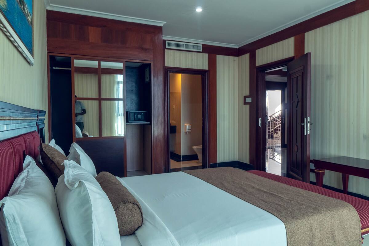 A hotel room with a bed, a wooden headboard, a television, and a sliding door leading to a balcony.