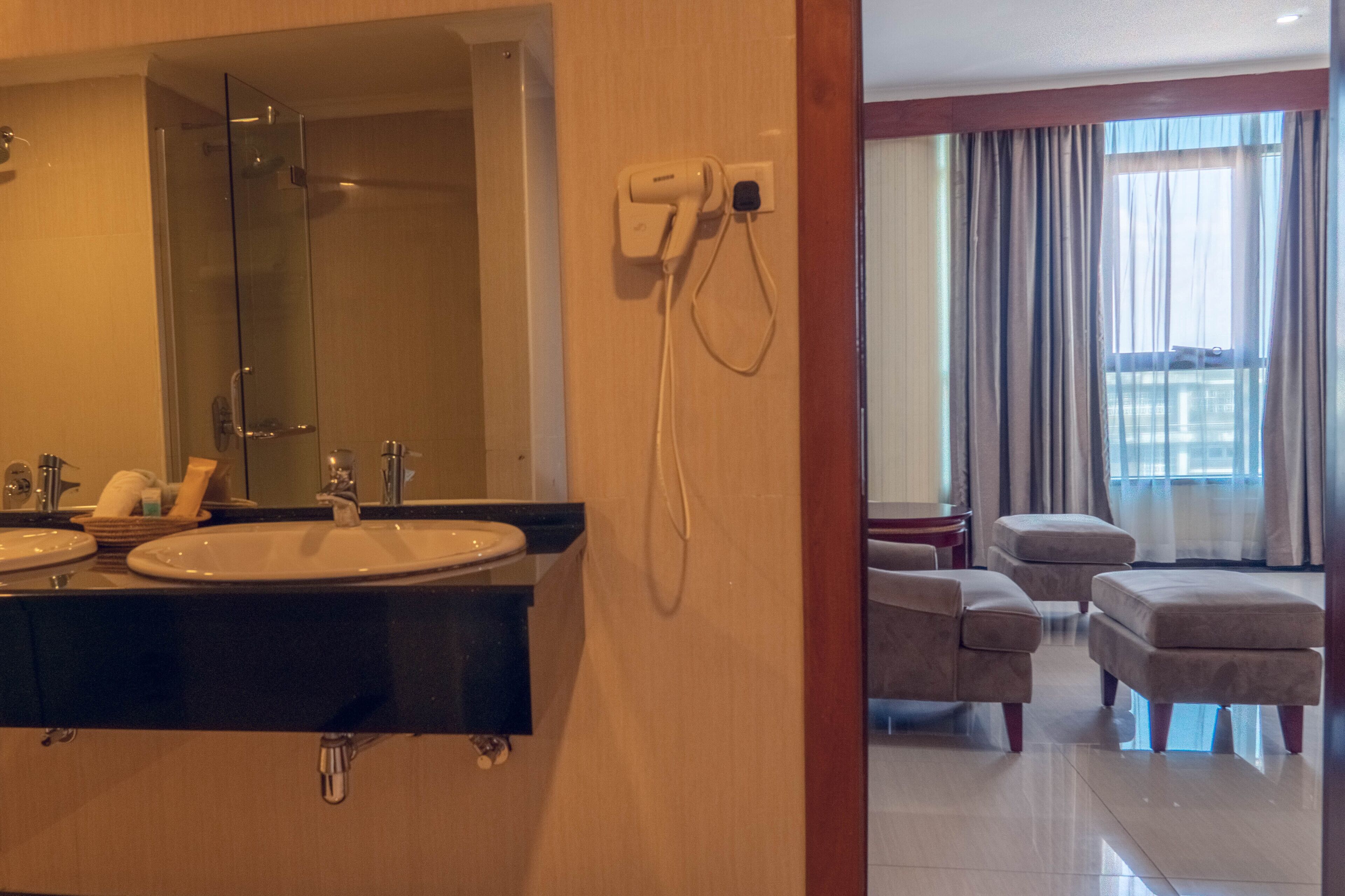 Ein Hotelbad mit zwei Waschbecken, einer Duschkabine aus Glas und einem an der Wand montierten Föhn.