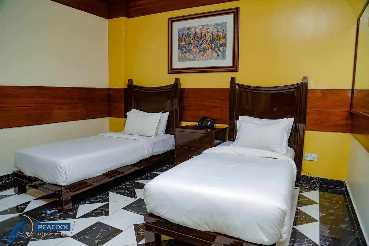 A hotel room with two single beds, a nightstand with a phone, a painting on the wall, and a checkered floor.